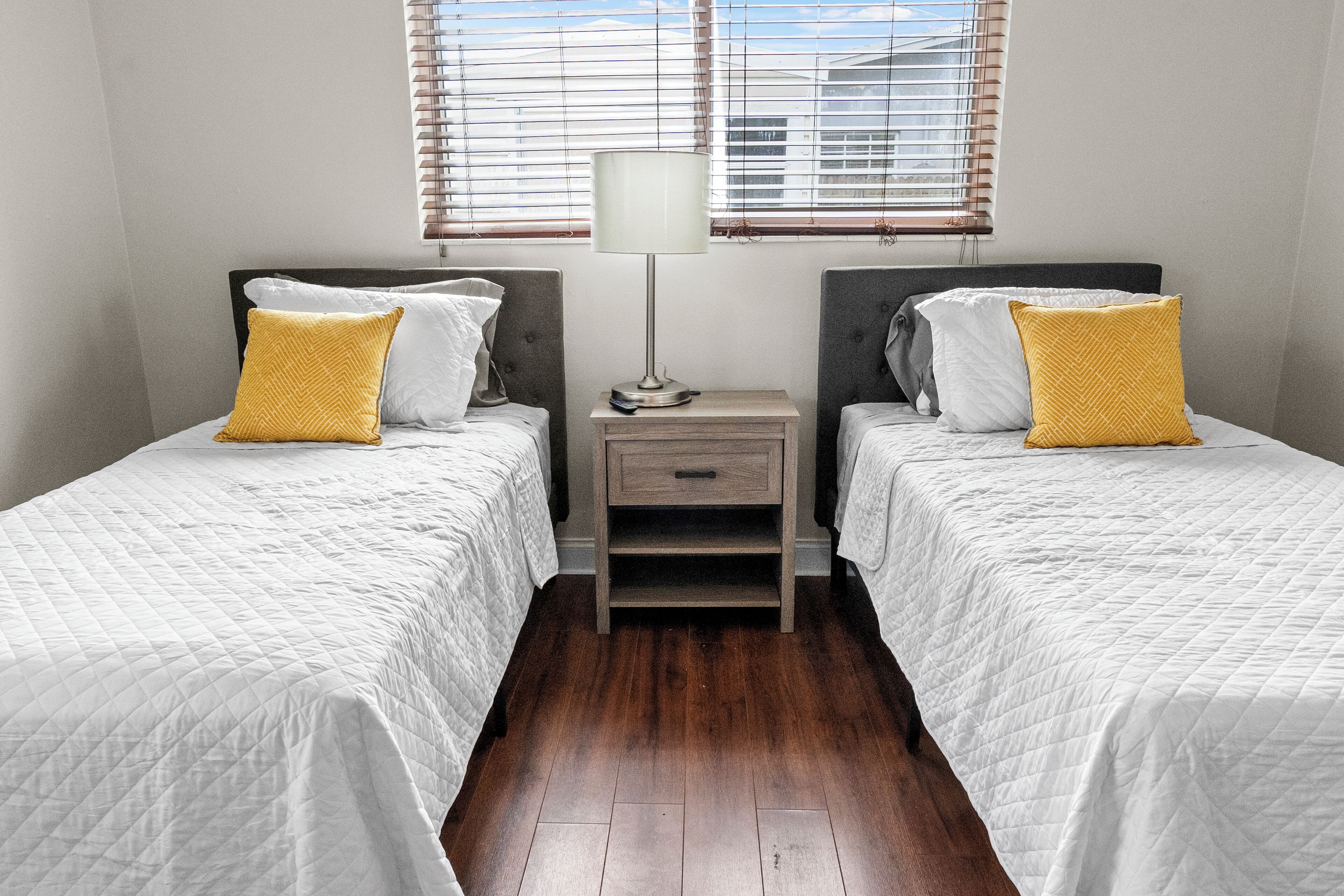 A bedroom with two beds, a nightstand, a lamp, and a window with blinds.