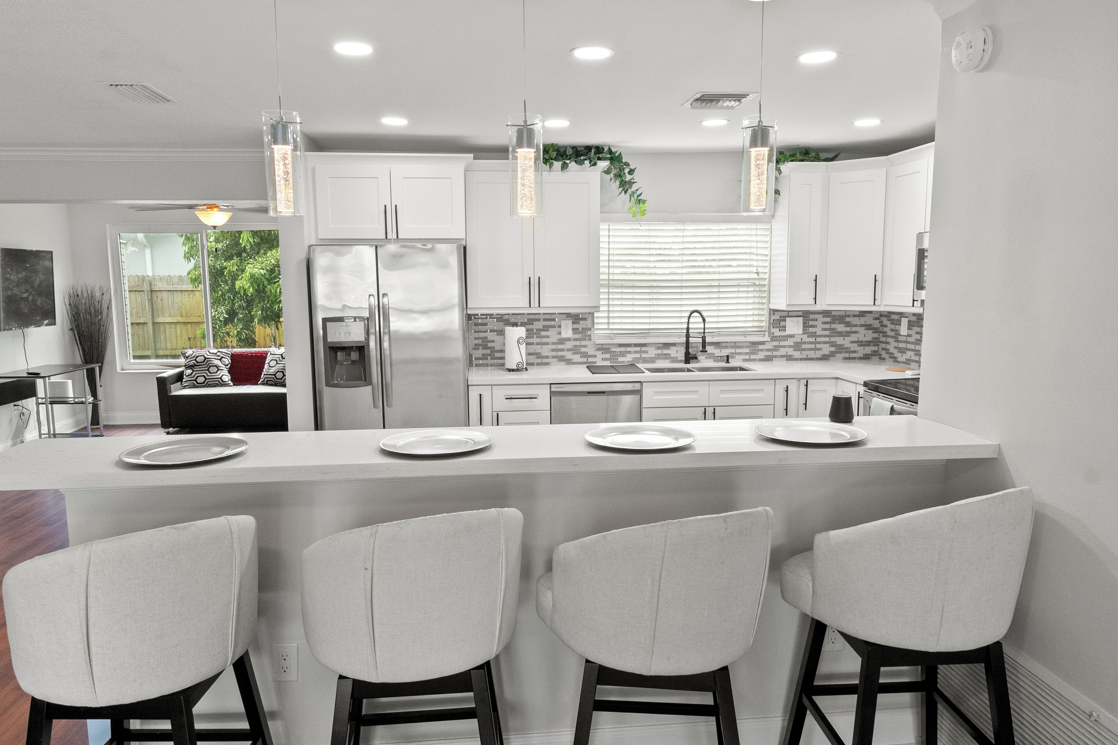 Una cocina moderna con gabinetes blancos, una isla central con taburetes altos e iluminación colgante.