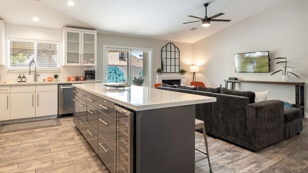 A modern kitchen with white cabinets, a central island, and a dining area with a sofa. - FoxTrotter | Scottsdale Pool Retreat | Sleeps 12 (Scottsdale)