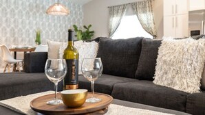 A modern living room with a dark grey sofa, a fluffy white throw pillow, a wine bottle, and two wine glasses on a wooden tray. - FoxTrotter | Scottsdale Pool Retreat | Sleeps 12 (Scottsdale)