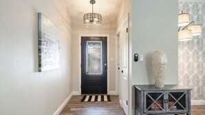 A hallway with a black door, a striped rug, a hanging light fixture, and a console table with decorative items. - FoxTrotter | Scottsdale Pool Retreat | Sleeps 12 (Scottsdale)