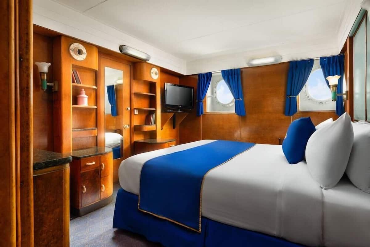 Une chambre à coucher avec un lit, des armoires en bois, une télévision et une fenêtre avec des rideaux.