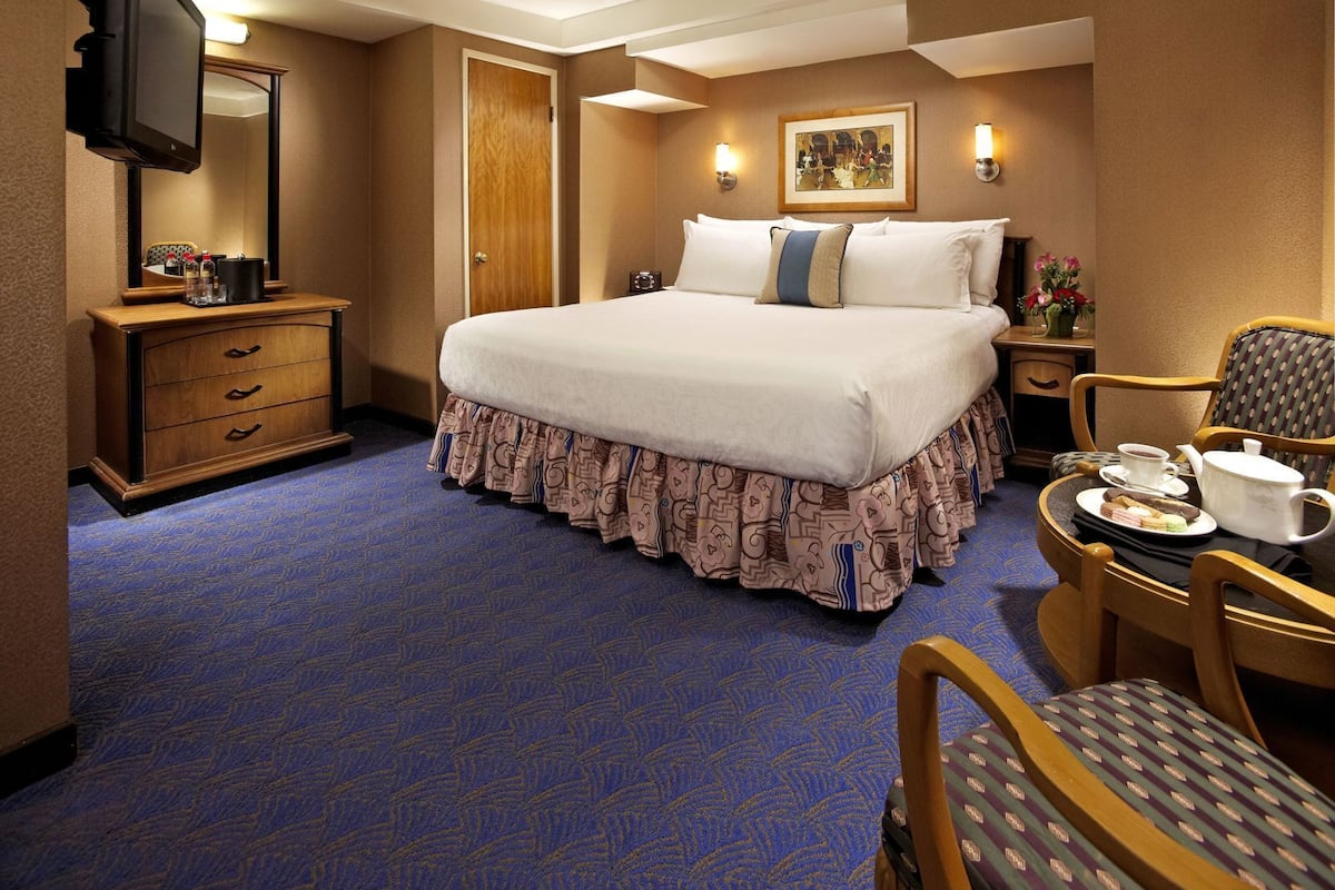 Une chambre d’hôtel comprenant un lit, un bureau avec une chaise, une télévision, une commode et un tableau au mur.