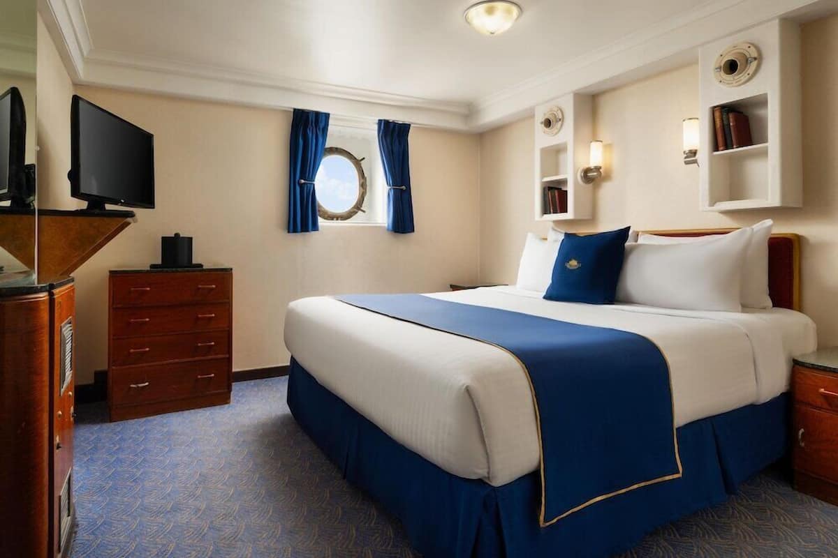 Une chambre d’hôtel comprenant un lit, une télévision, une commode, une fenêtre avec des rideaux et une bibliothèque.