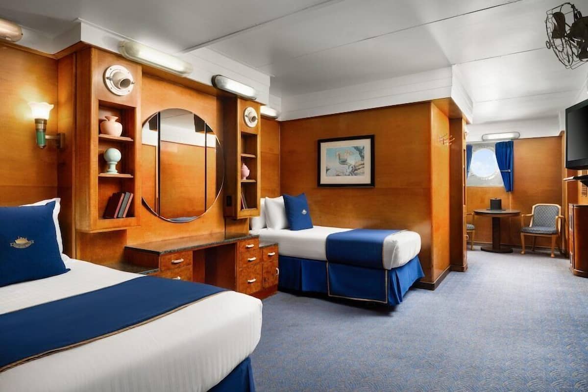 Une chambre d’hôtel avec deux lits, un bureau, une chaise, une télévision et un tableau encadré au mur.