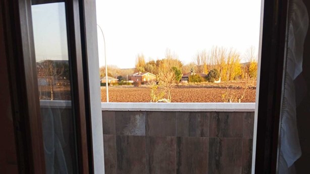 A view through a glass door into a patio area with a stone floor, a low wall, and a field in the background.