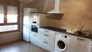 A compact kitchen with a built-in oven, microwave, and washing machine, a sink, and a window with blinds.