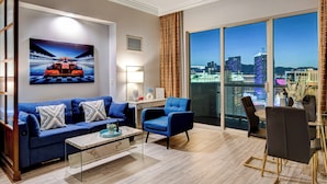 Un salon moderne avec vue sur la ville, comprenant un canapé, des fauteuils, une table basse et un coin repas.