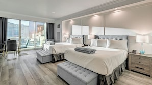 Une chambre d’hôtel moderne avec deux lits, un grand miroir, un balcon offrant une vue sur la ville et un bureau avec une lampe.