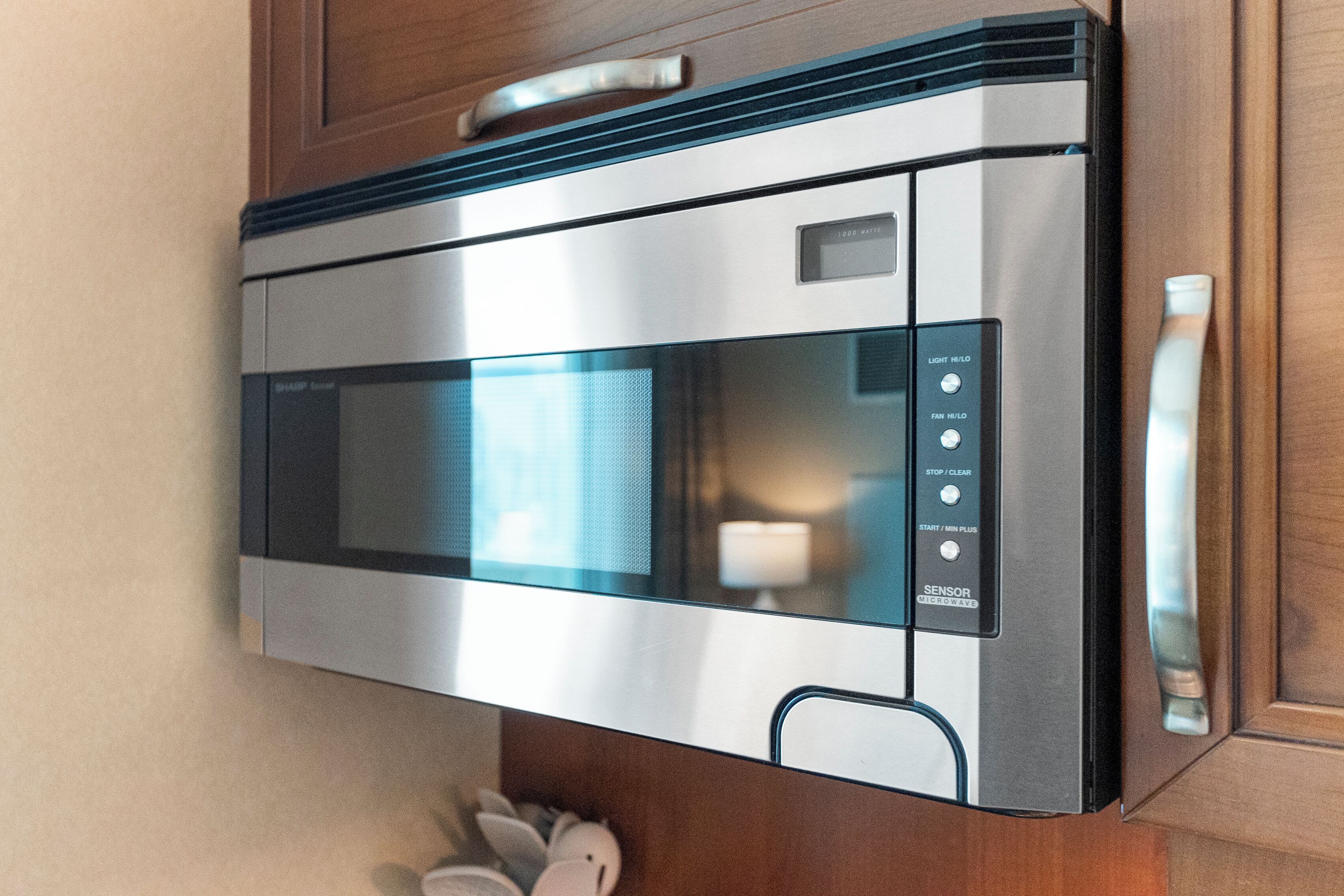 Un four à micro-ondes en acier inoxydable doté d’un écran numérique et d’un panneau de commande, installé dans une cuisine avec des meubles en bois.
