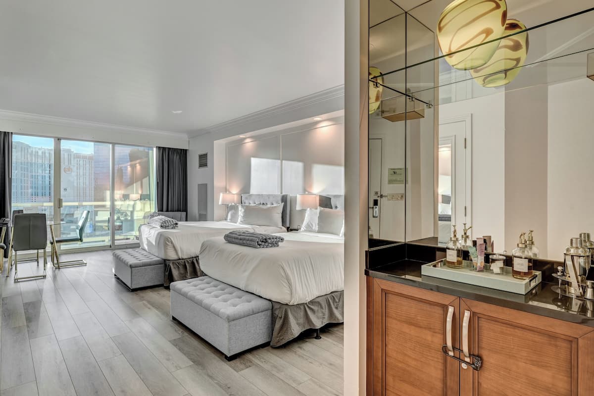 Een hotelkamer met een groot bed, een zithoek, een balkon met uitzicht over de stad, en een moderne badkamer met wastafel.