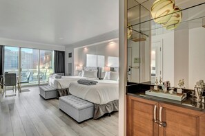 Et hotelværelse med en stor seng, et siddeområde, en balkon med udsigt over byen og et moderne badeværelse med vask.