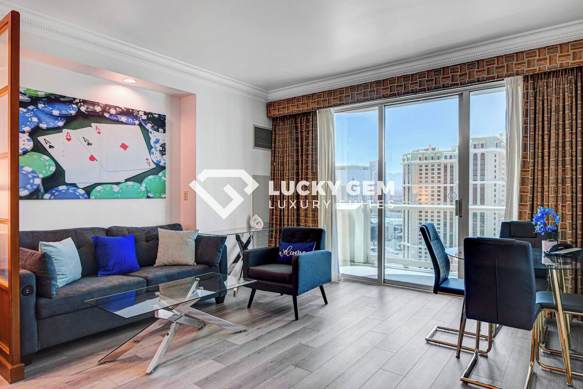 Een moderne woonkamer met een bank, fauteuils, een glazen salontafel en uitzicht op de stad door grote ramen.