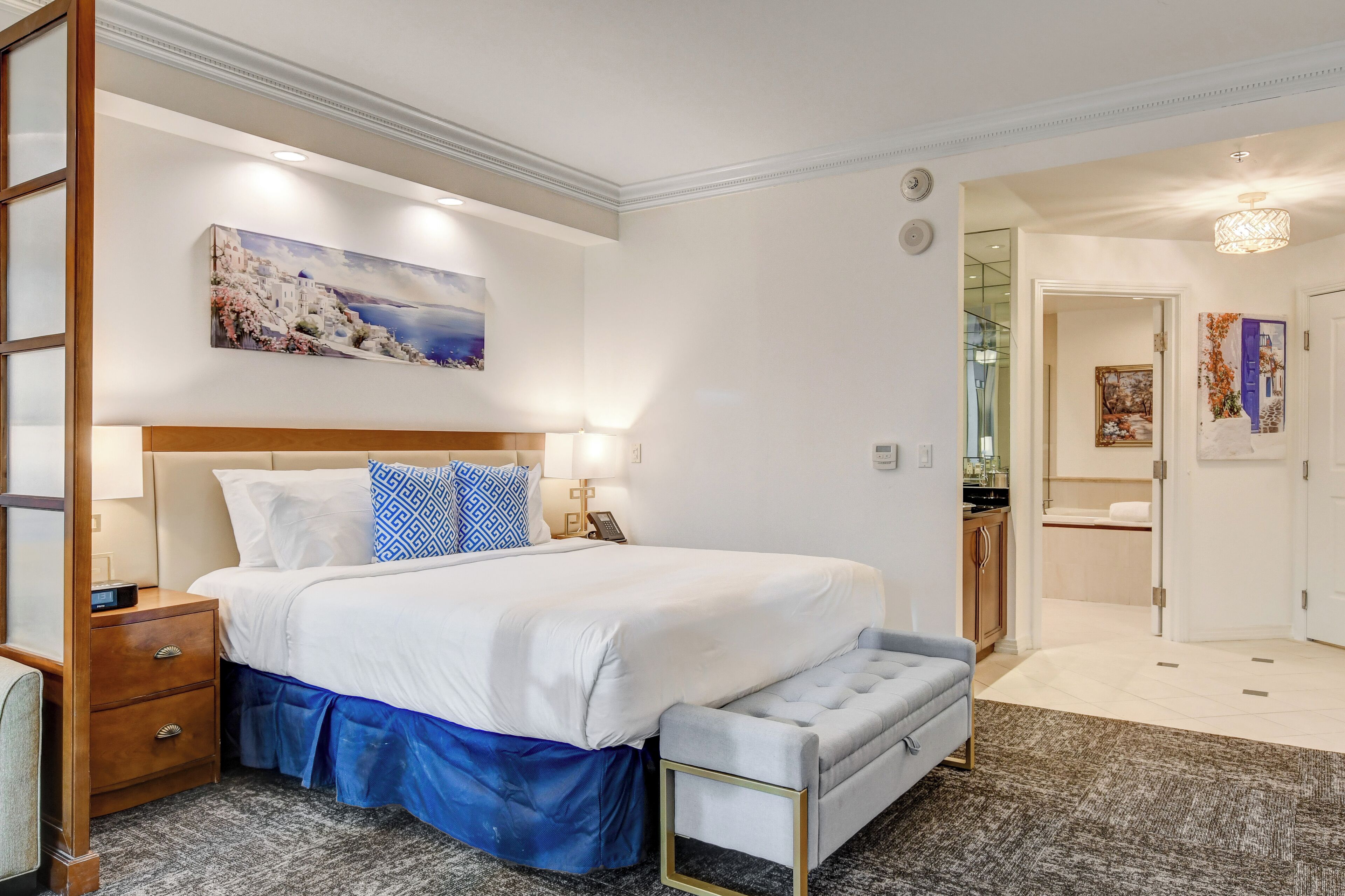 A hotel room with a bed, bedside table, and a painting on the wall.