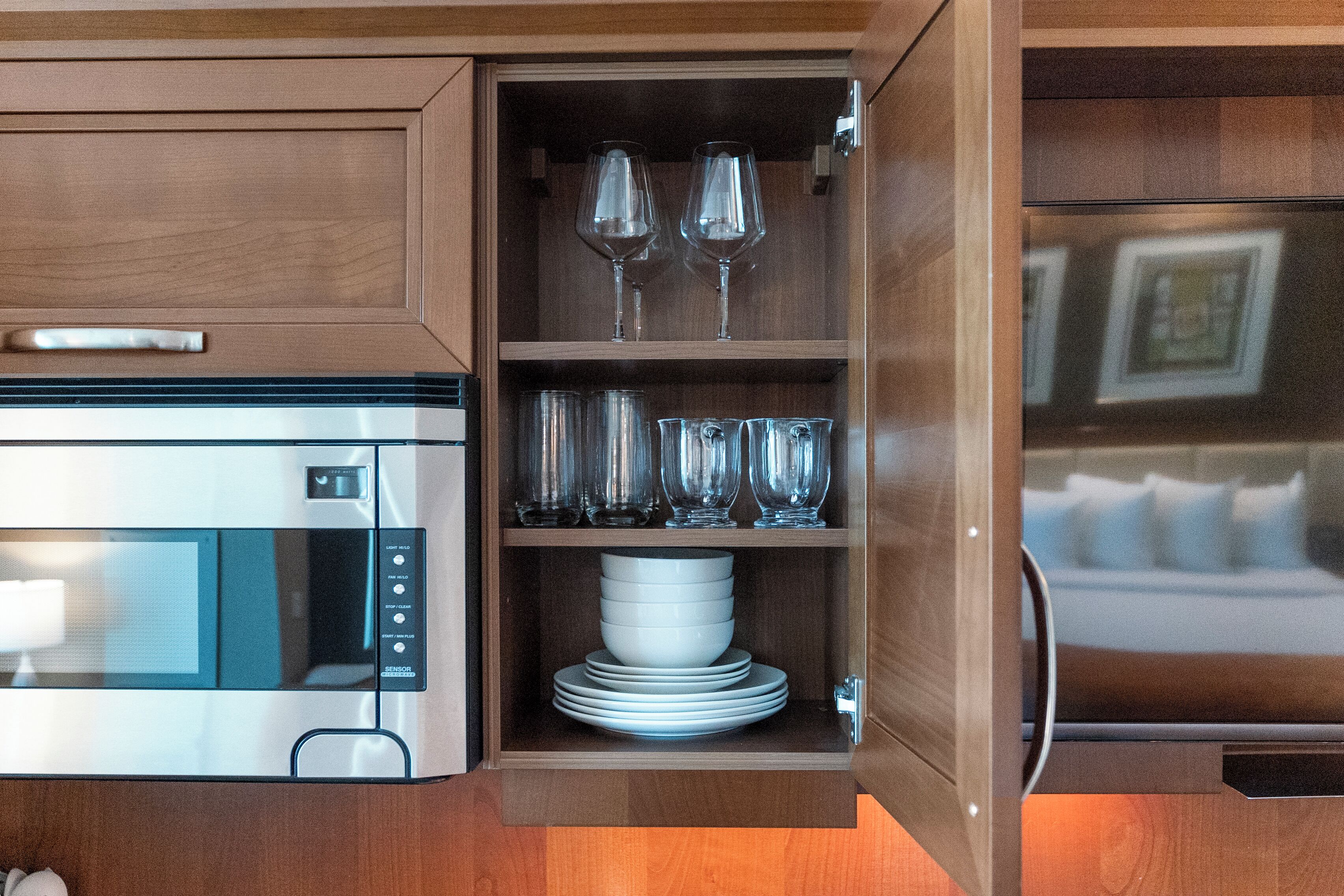 Une cuisine compacte équipée d’un four à micro-ondes, d’un four encastré et d’un meuble en bois contenant de la vaisselle et des verres.