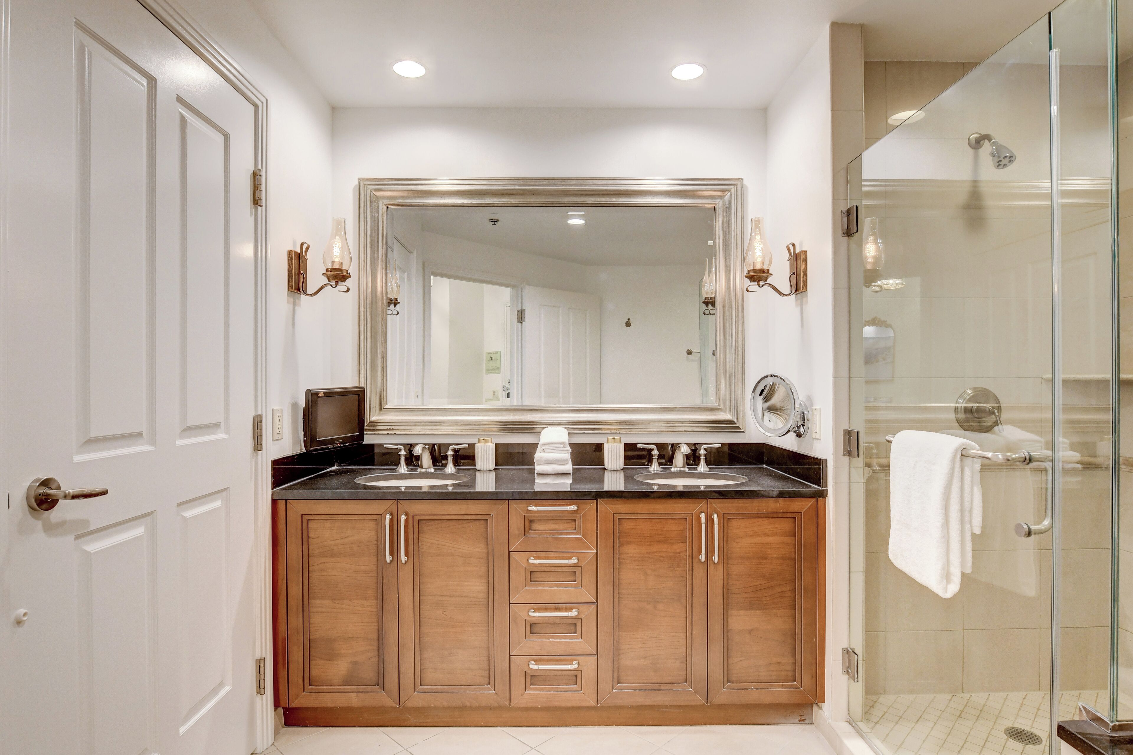 A bathroom with a double sink vanity, a large mirror, and a glass-enclosed shower.
