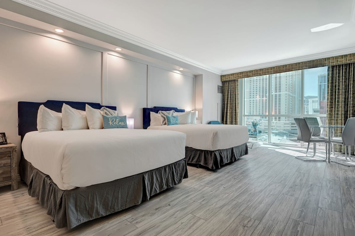 Een hotelkamer met twee bedden, een bureau en een groot raam met uitzicht op de stad.
