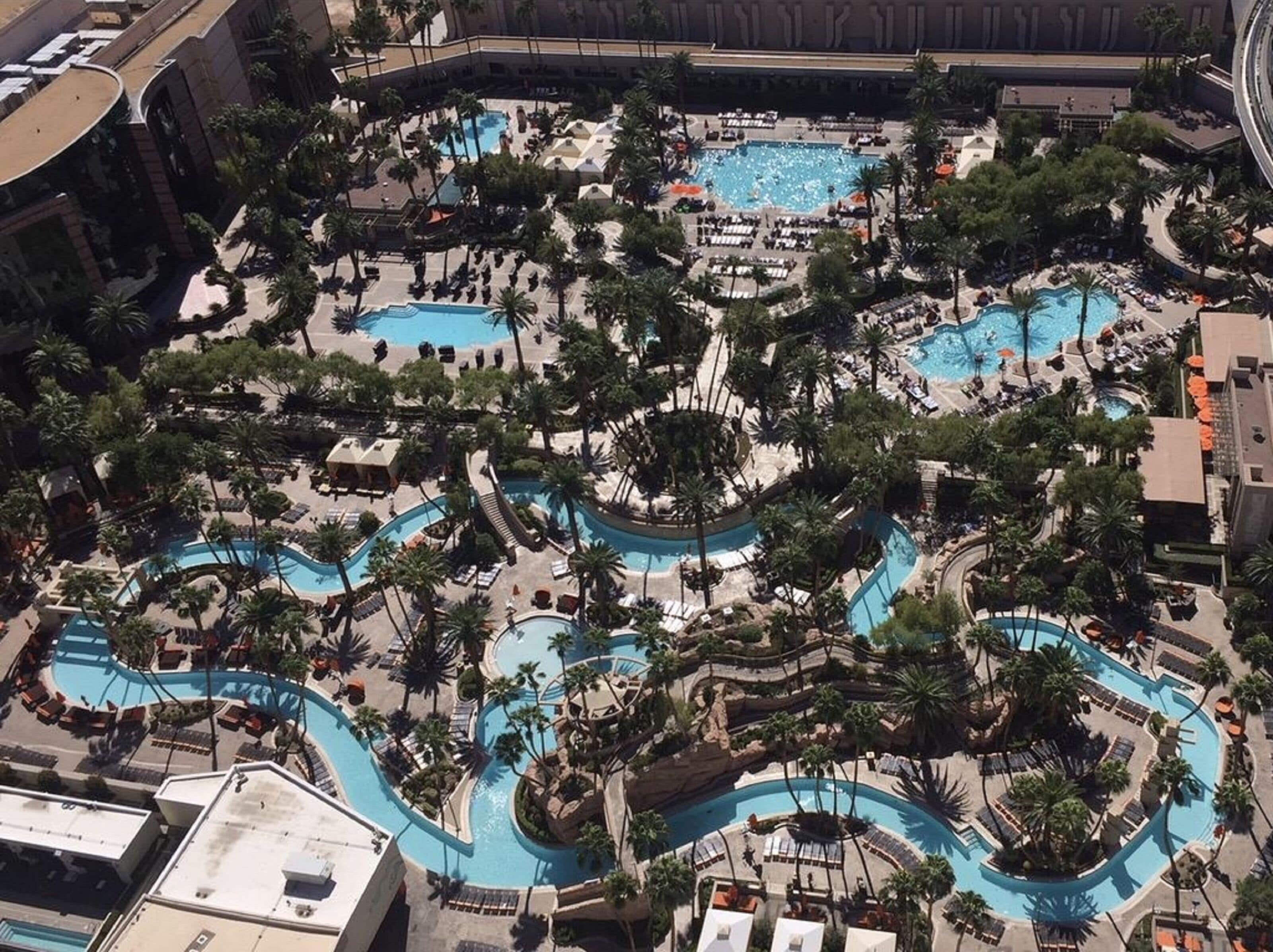 An aerial view of a resort with multiple swimming pools surrounded by palm trees and lounge areas.
