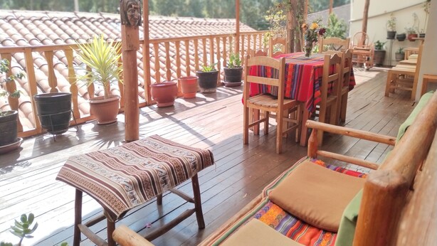 Um deck de madeira com mesa e cadeiras, rodeado por plantas em vasos e um corrimão de madeira.