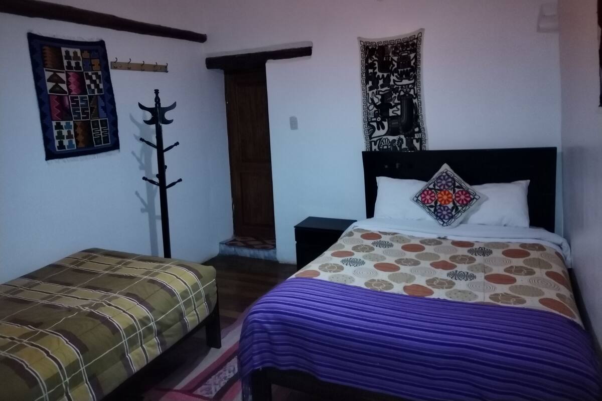 A bedroom with a bed, a nightstand, a chair, a coat rack, and a door.