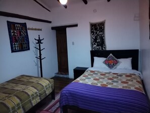 Un dormitorio con cama, mesita de noche, silla, perchero y puerta.