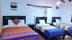 Quarto de hotel com três camas, cada uma com uma colcha de padrão diferente. Há cabeceiras e mesas de cabeceira de madeira com luminárias.