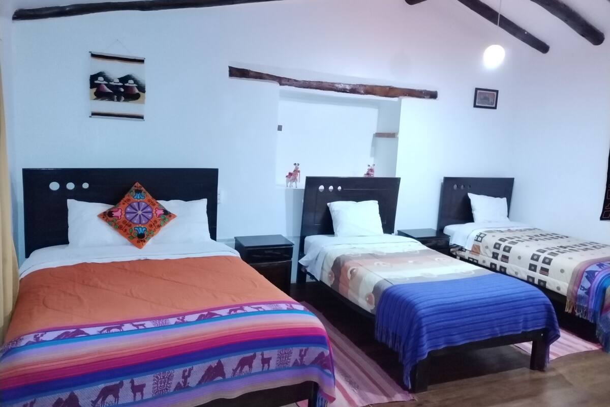 A hotel room with three beds, each with a different patterned bedspread. There are wooden headboards and nightstands with lamps.