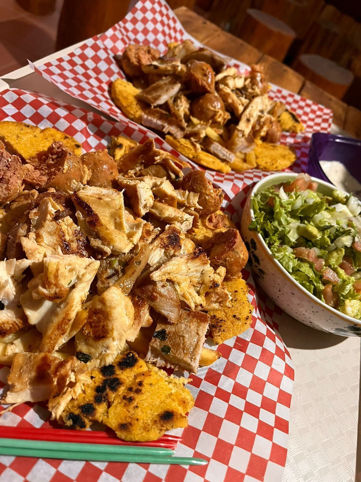 A meal consisting of grilled chicken, fried plantains, and a side salad on a checkered tablecloth.