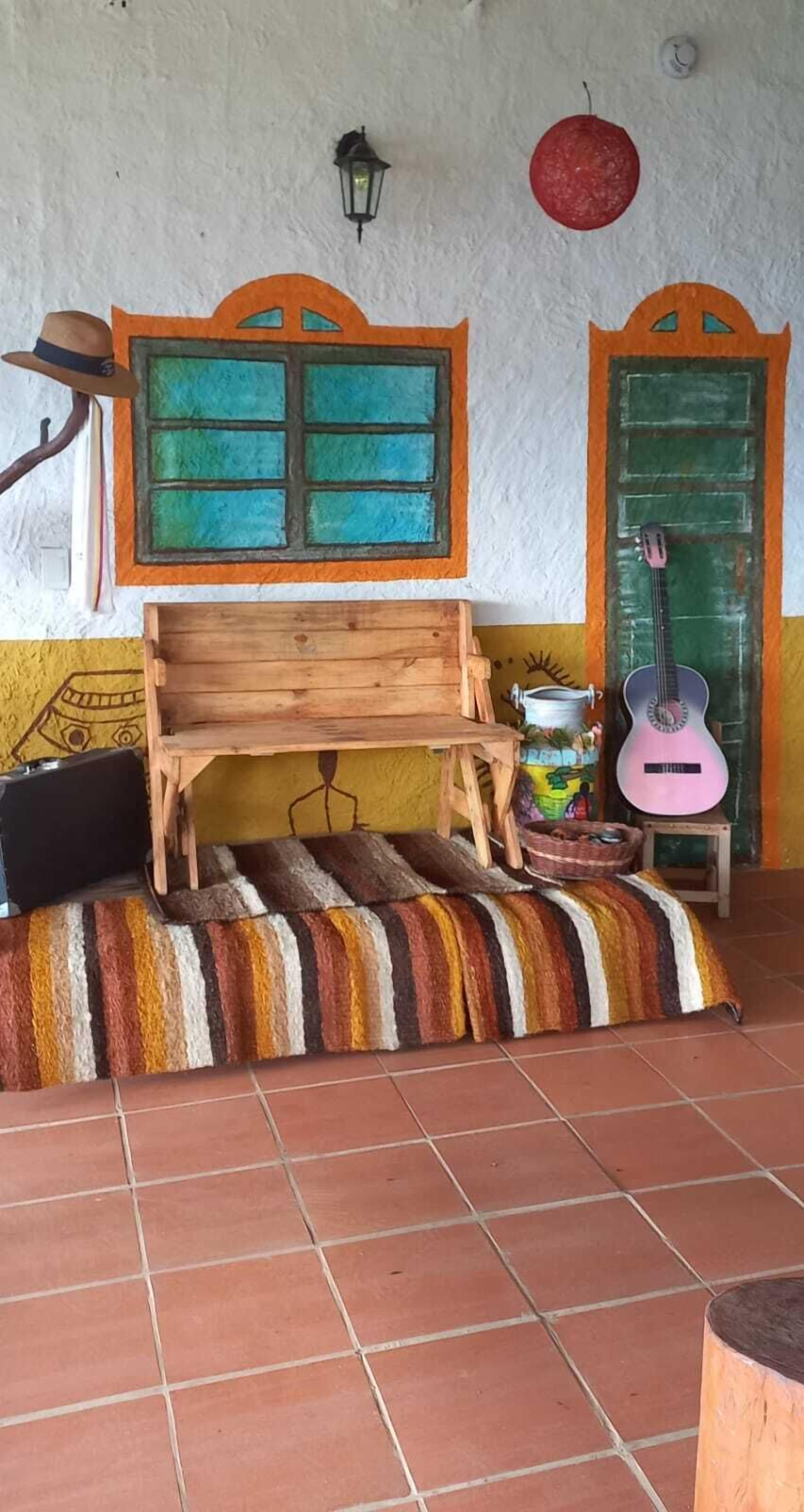 Una habitación con un banco de madera, una guitarra, un farol y una puerta con marco verde.
