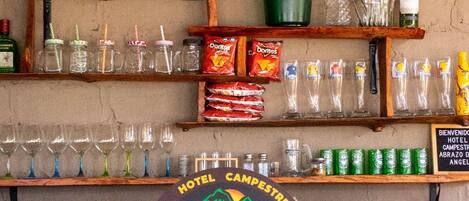 Zona de bar con estantes de botellas y vasos, un letrero que dice 'TERRITORIO GUANEE' y un logotipo de 'ABRAZO del ANGEL CAMPING - PICNIC'.