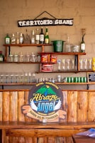 Una zona de bar con estantes llenos de botellas, vasos y aperitivos. Un letrero dice 'Territorio Guane'.
