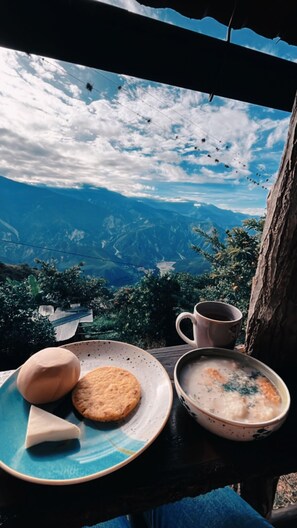 Una mesa con un plato de comida, una taza y vistas a un paisaje montañoso.