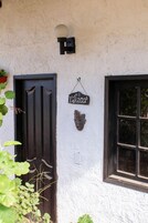 Un edificio rústico con una puerta negra y una ventana. Se ve un letrero en la pared que dice “Pizza.”