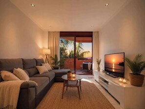 A living room with a sofa, a coffee table, a TV, and a view of the outdoors.