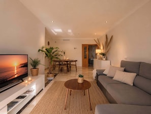 A living room with a TV, sofa, coffee table, and dining area.