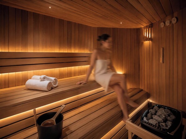 A sauna room with wooden benches, towels, a bucket, and a tray of stones.