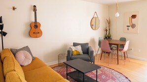 Een woonkamer met een bank, fauteuil, salontafel, eettafel met stoelen, een gitaar, een spiegel en een hanglamp.