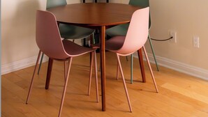 Een eethoek met een ronde tafel, vier stoelen, een hangende lamp, een ronde spiegel en twee vazen met gedroogde planten.
