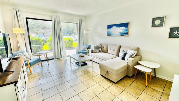 Ein geräumiges Wohnzimmer mit einer Couch, einem Couchtisch und einem kleinen runden Tisch. Ein Glastür öffnet sich zu einem Balkon mit Blick ins Freie.
