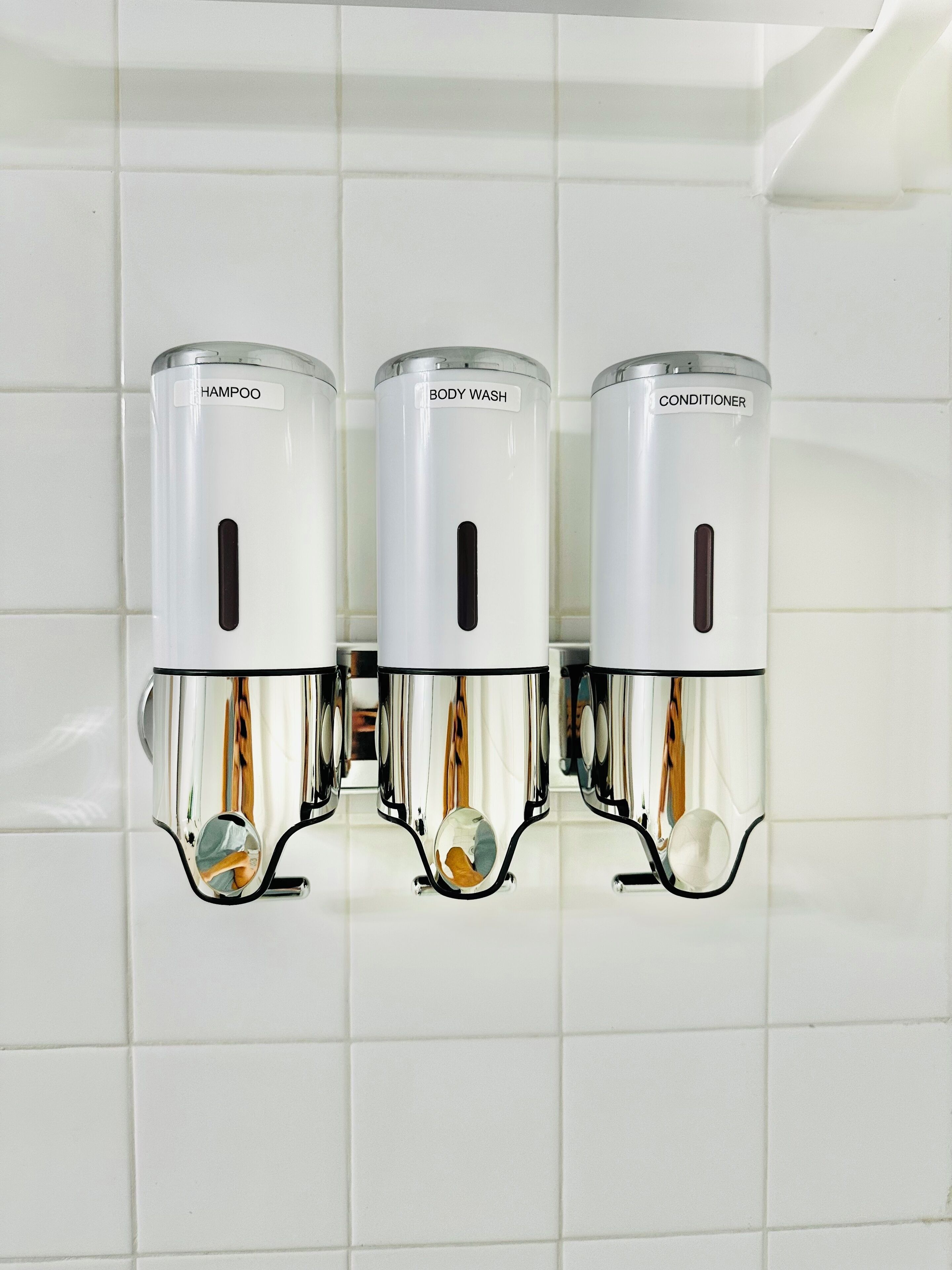 Three wall-mounted dispensers labeled "HAMPOO," "BODY WASH," and "CONDITIONER" in a bathroom setting.