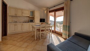 A compact kitchen with a dining area, a sofa, and a balcony with curtains.