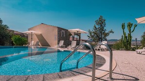 A swimming pool with a stone wall, lounge chairs, and a building with arches.