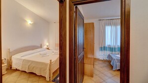 A bedroom with a bed, bedside table, and a door leading to another room.