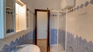 A bathroom with a sink, mirror, shower, and tiled walls.