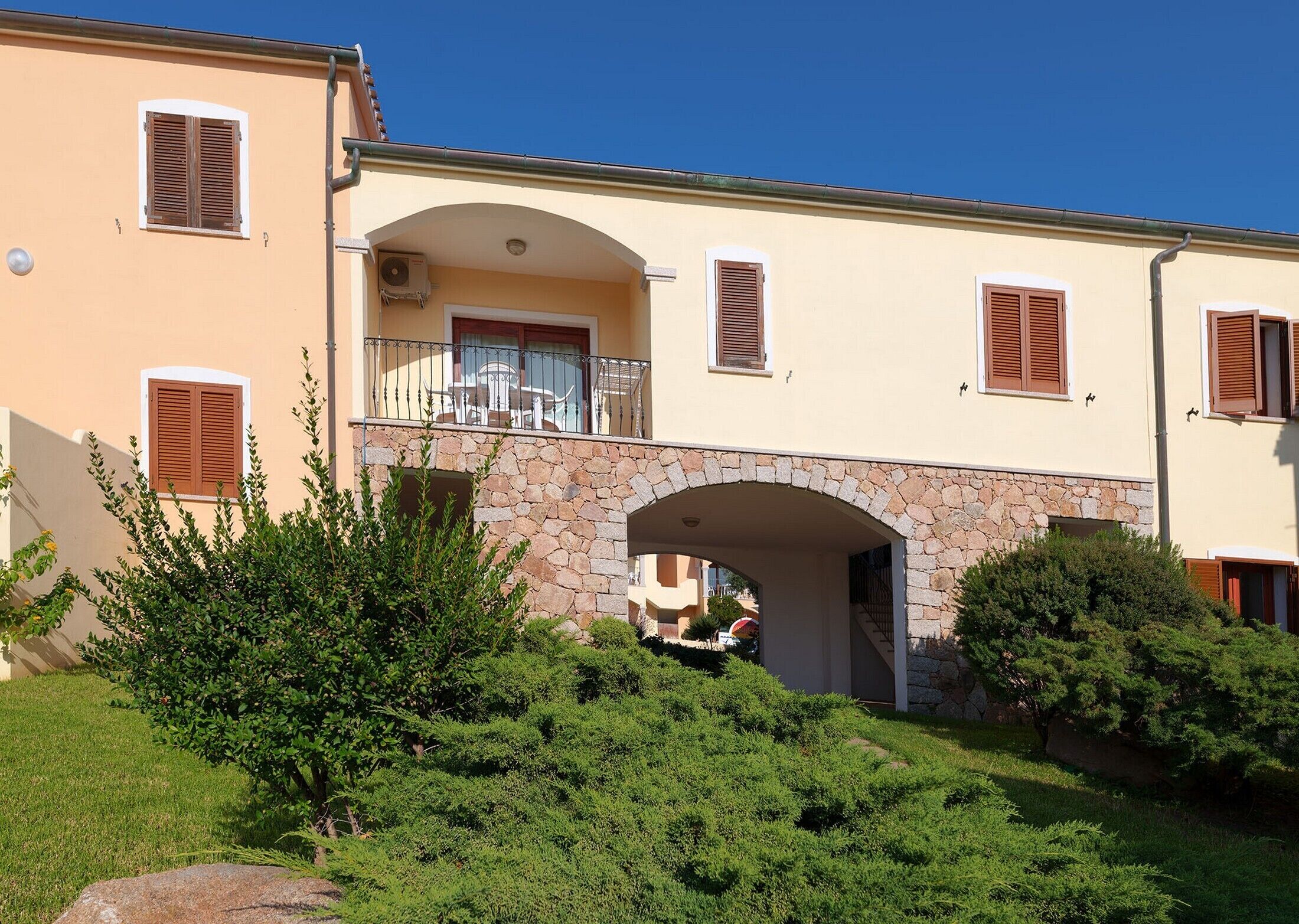 A two-story building with a stone archway entrance, balconies with railings, and a clear blue sky.