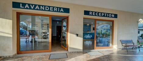 Entrada de hotel con carteles que indican 'LAVANDERIA' y 'RECEPTION', un banco y vistas de una montaña a través del ventanal de recepción.