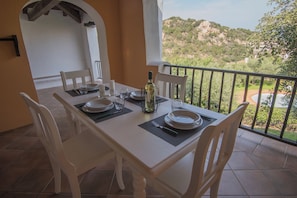 Una mesa de comedor dispuesta con platos, vasos y una botella, con vistas a un paisaje pintoresco.