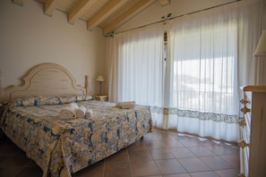 Un dormitorio con cama, mesita de noche, lámpara y ventana con cortinas.