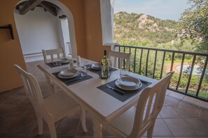 Mesa lista con platos, vasos y una botella, con vistas a un paisaje montañoso.