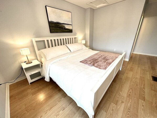 Une chambre à coucher avec un lit, des tables de chevet, une lampe, un tableau et un plancher en bois.